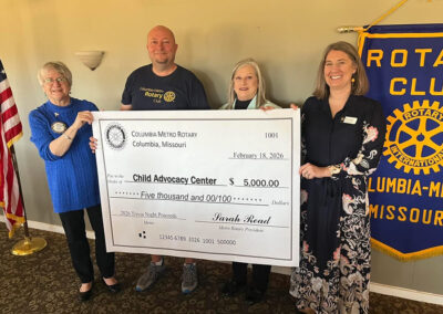 Four adults pose with an extra large check. A Rotary Club banner is off to one side.