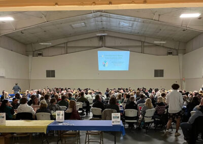 A presentation is displayed high on a wall in a hall with hundreds gathered to learn.