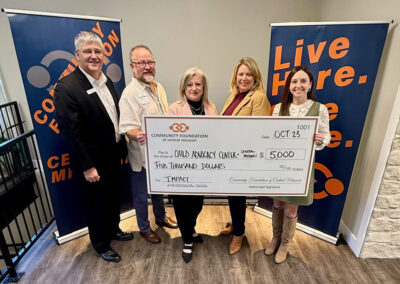 An oversized check presentation shows funds moving to CACCMO from Community Foundation of Central Missouri. Five adults pose for a photo op.