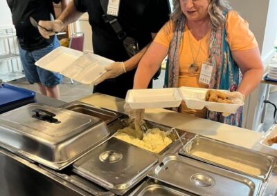 A few adults move through a food line, filling to-go trays.