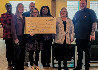 Seven adults gather around an oversized check presentation.